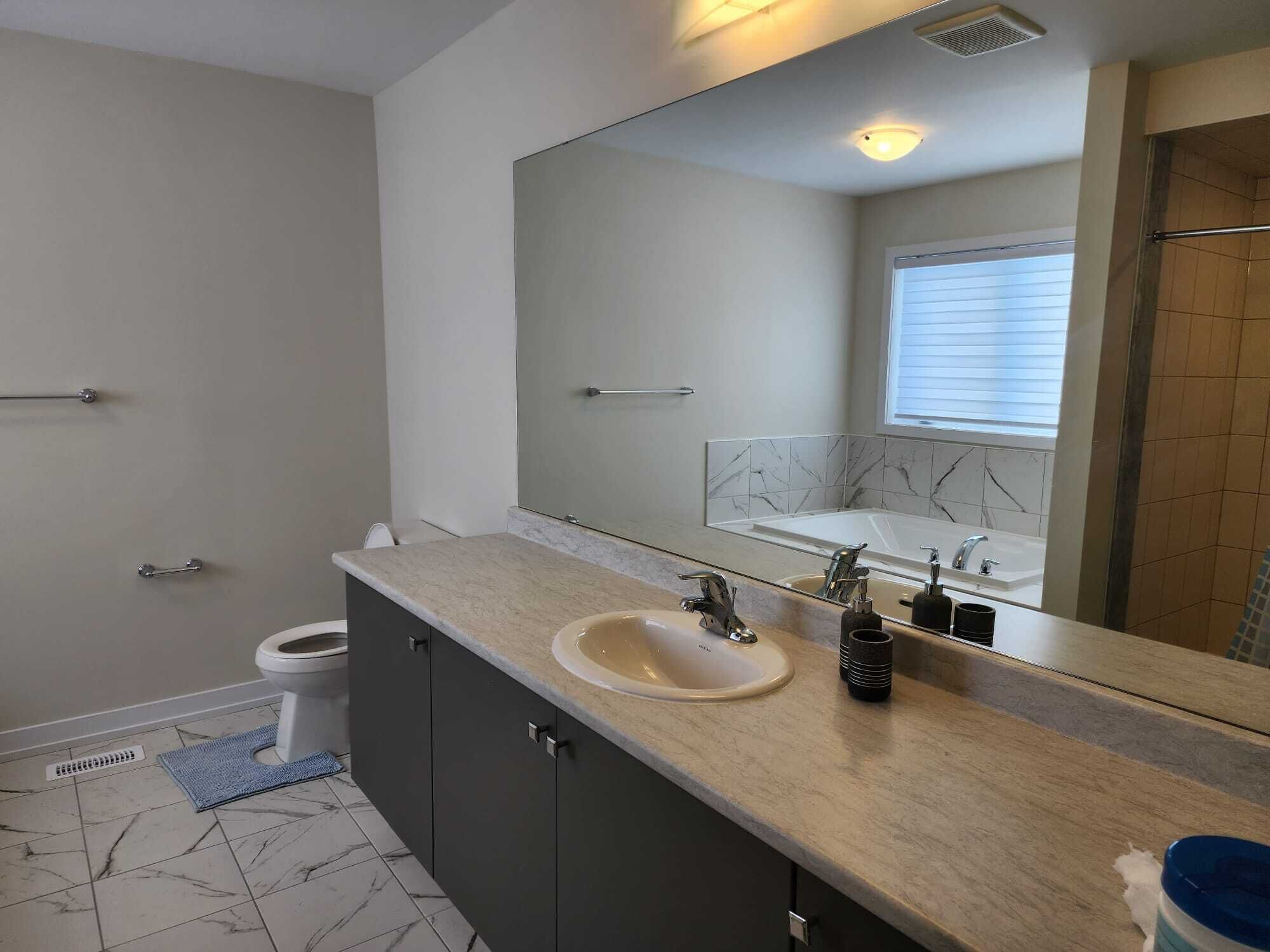 A modern bathroom with a marble-tiled floor, a large mirror, a sink with a faucet, and a toilet.