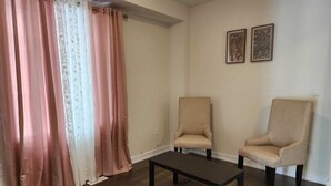 A room with two beige armchairs, a dark wooden coffee table, and a window with pink curtains. - Brand new home in Caledonia walking distance to river trail (Caledonia)