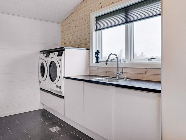 A laundry room with a front-loading washer and dryer, a sink, and a window with blinds.