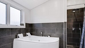 A modern bathroom with a freestanding bathtub, dark tiled walls, and a shower area. - 5 Star Holiday Home in Hejls (Hejls)