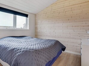 A bedroom with a bed, a window, wooden panel walls, and a wooden floor.