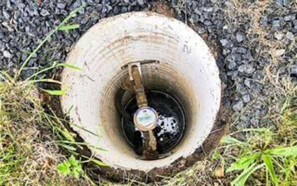 A manhole cover with a metal object inside, surrounded by gravel and grass.