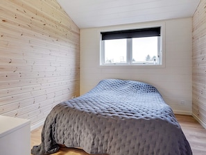A room with a bed, wooden walls, a window, and a view of the outside.