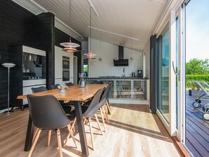 A modern kitchen with a large island, black cabinetry, and a glass-enclosed dining area with a wooden table and chairs.