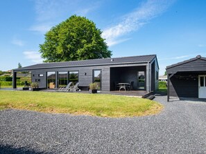 A modern house with a covered patio, a garage, and a large tree in the background.
