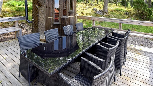 Une terrasse dotée d’une table à plateau en verre, entourée de chaises en osier, d’un gazebo en bois et d’une balustrade en bois.