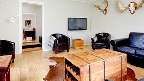 Un salon avec une table basse en bois, des canapés en cuir, un téléviseur et des éléments de décoration murale en forme de bois de cerf.