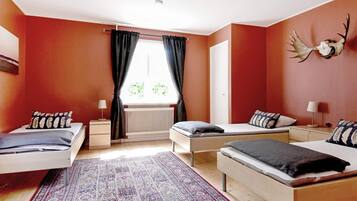 A bedroom with two single beds, a large patterned rug, a radiator, and a deer skull on the wall.