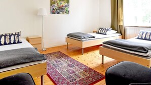Une pièce avec trois lits, une lampe sur pied, un tapis à motifs et un tableau accroché au mur.