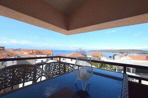 A balcony with a table and chairs, overlooking a coastal area with red-roofed buildings and the sea. - Holiday apartment in attic with sea view (Njivice)