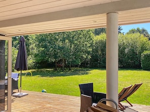 Un patio al aire libre con una terraza de madera, una mesa, sillas y una hamaca.