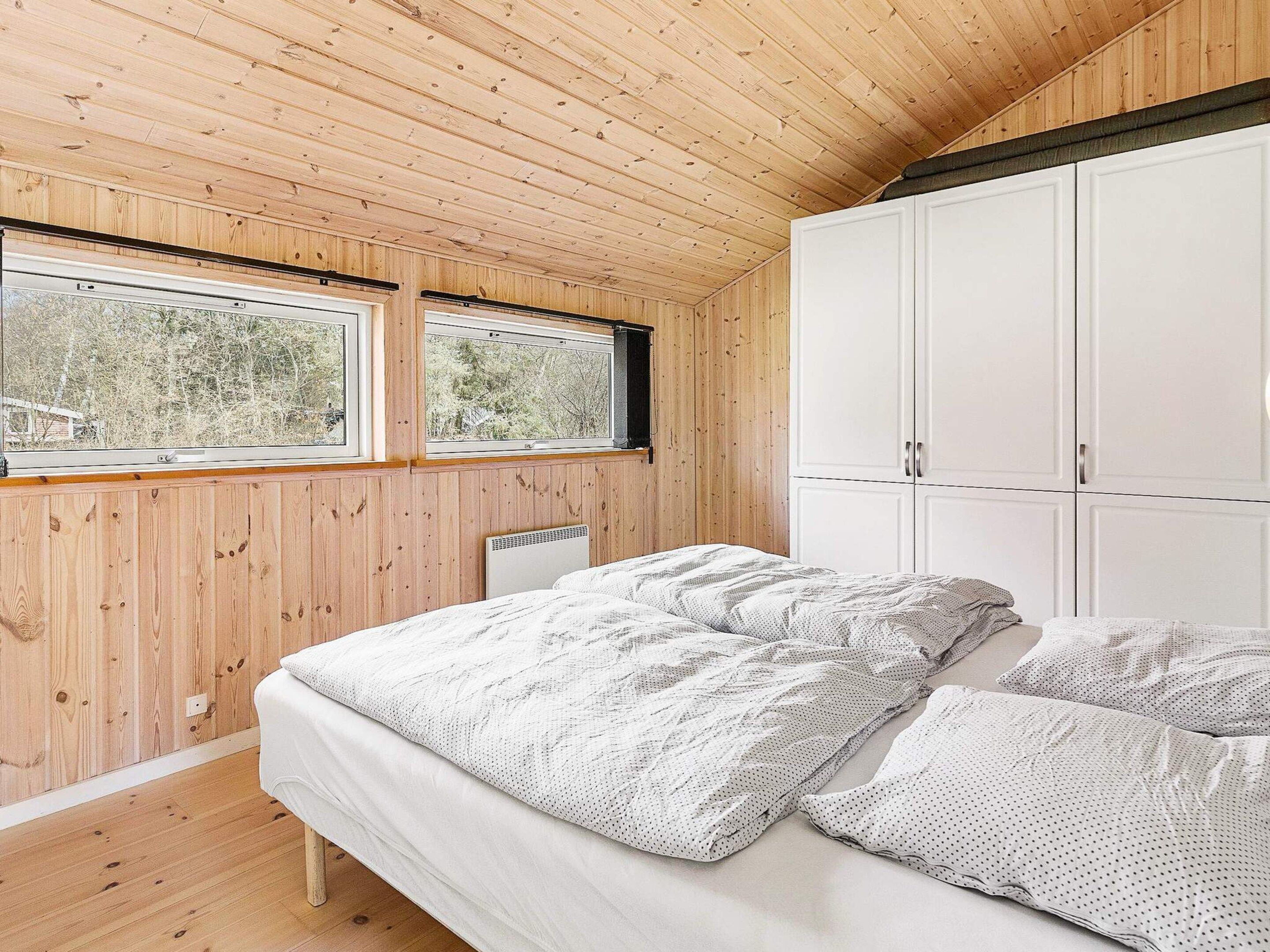 A bedroom with a bed, two windows, a radiator, and a wardrobe.