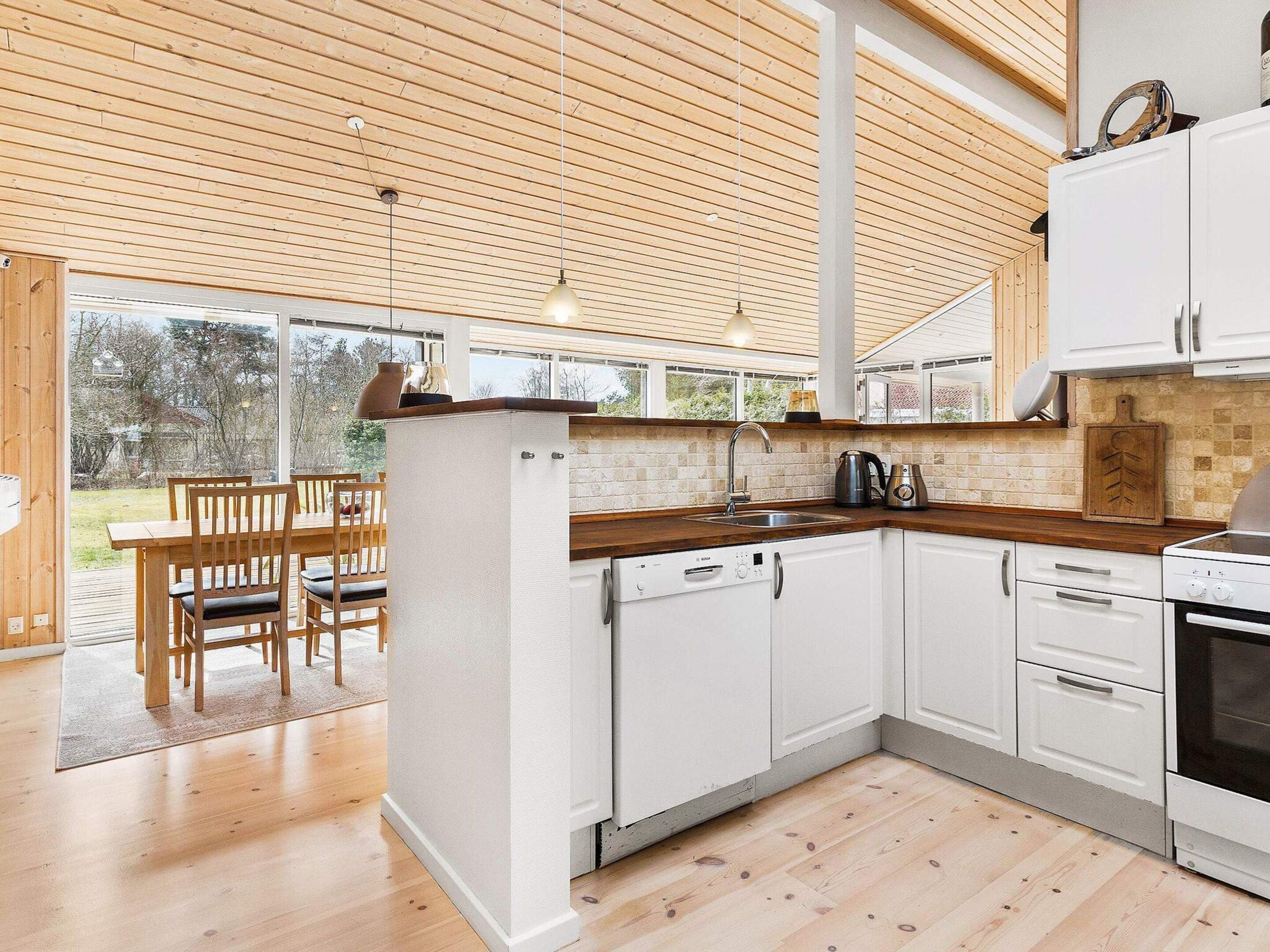 A modern kitchen with white cabinetry, a wooden countertop, and a view of the outdoors through large windows.