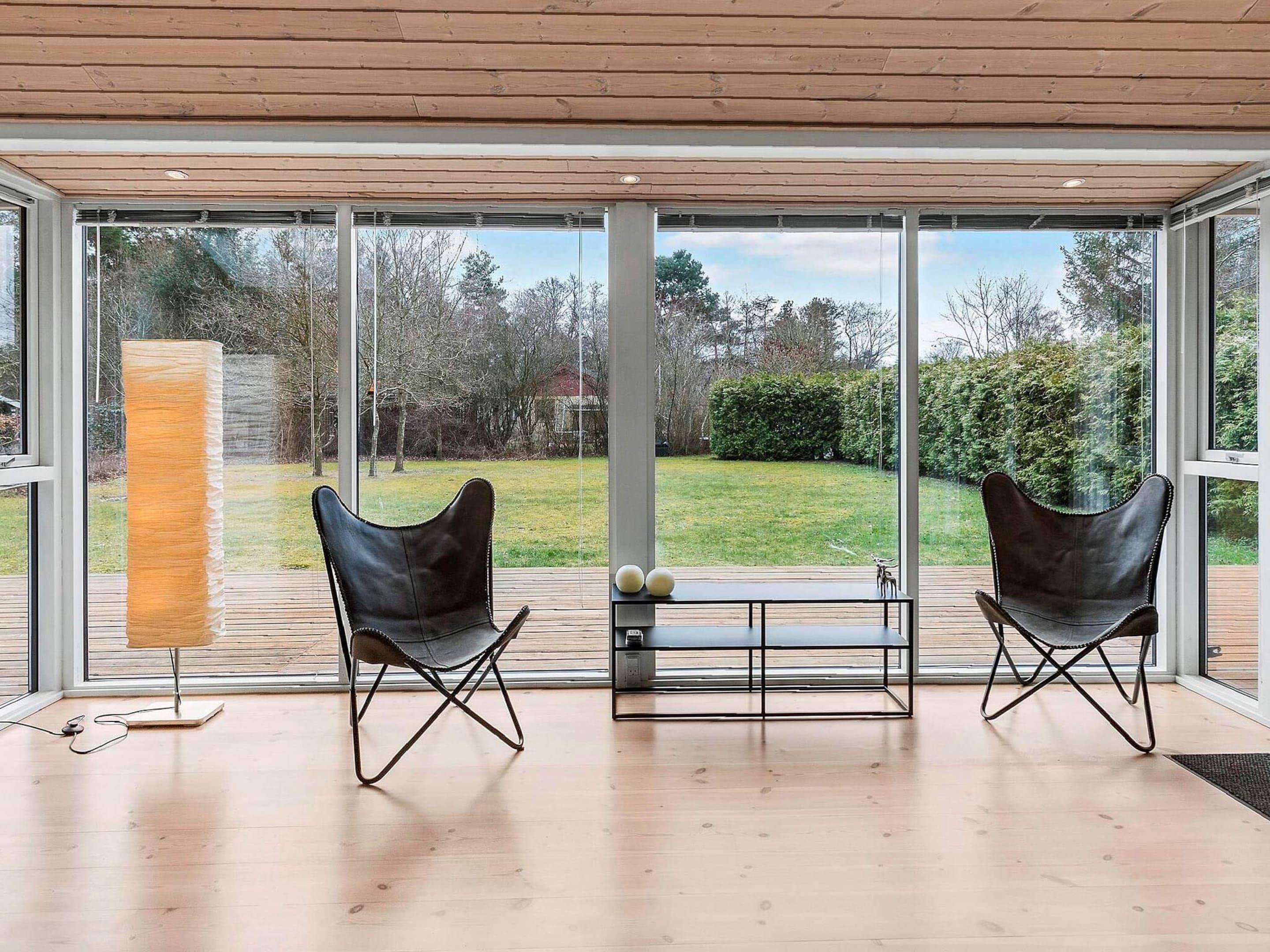 Een modern interieur met twee leren fauteuils gericht op een groot raam, een houten plafond en een kleine tafel met decoratieve objecten.