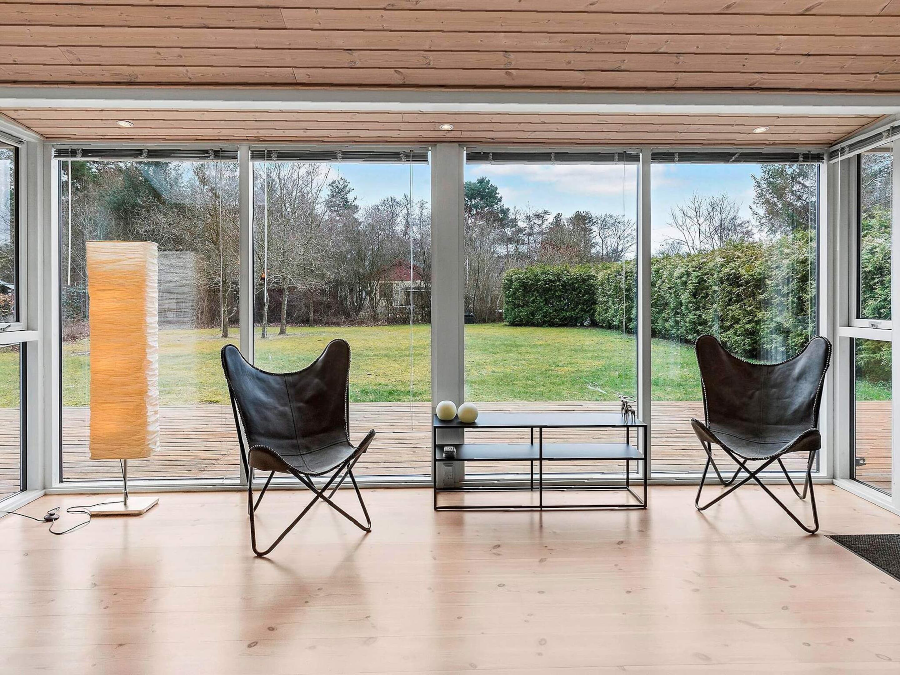 A modern room with large glass windows, two leather chairs, a wooden floor, and a small table with decorative balls.