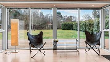 A modern room with large glass windows, two leather chairs, a wooden floor, and a small table with decorative balls.