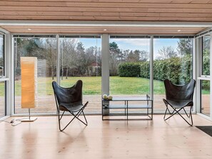 Una habitación moderna con grandes ventanales de vidrio, dos sillones de cuero, piso de madera y una pequeña mesa con bolas decorativas.