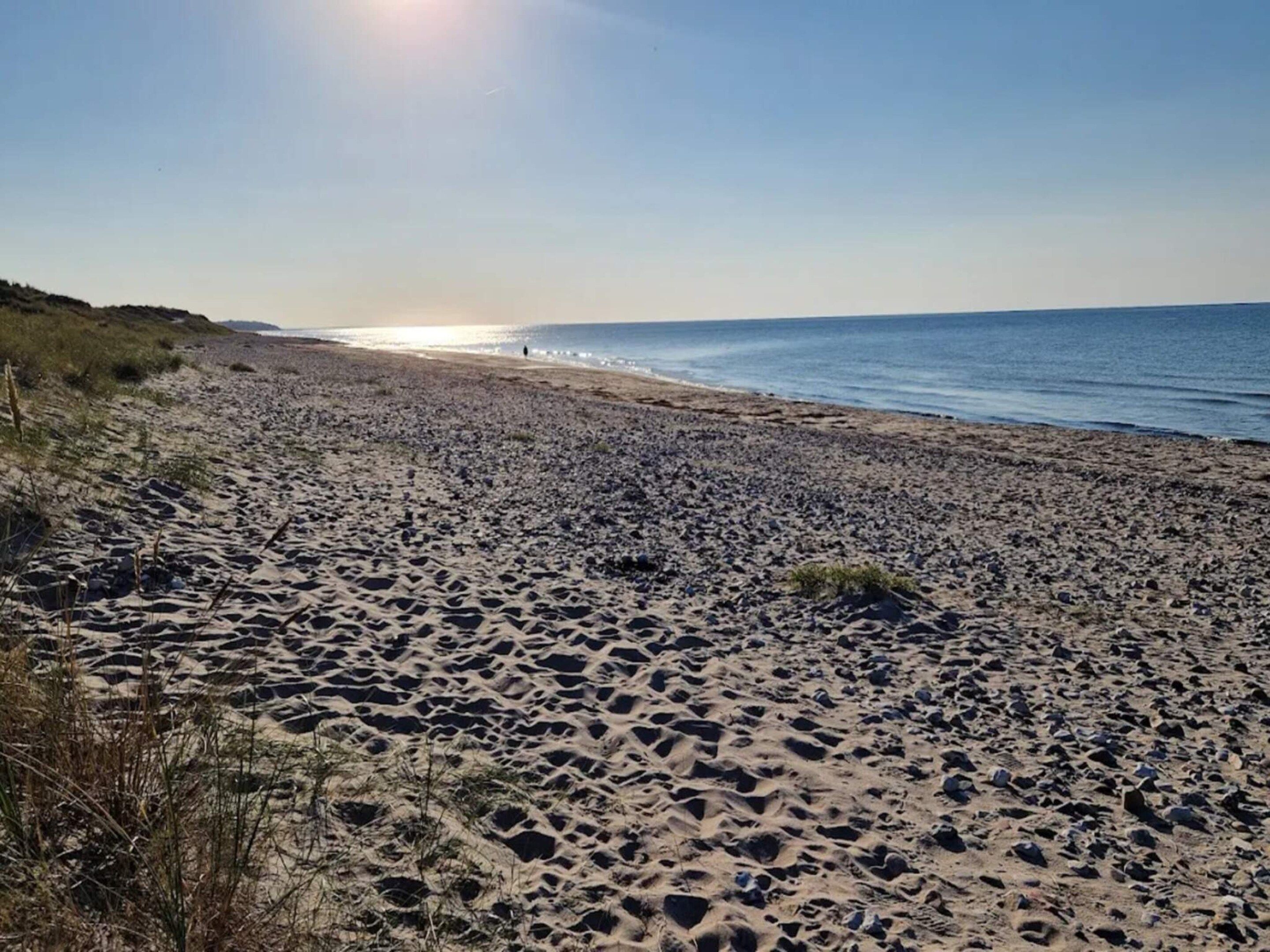 Een strand met een heldere lucht en de zon laag aan de horizon.