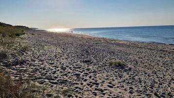 Een strand met een heldere lucht en de zon laag aan de horizon.