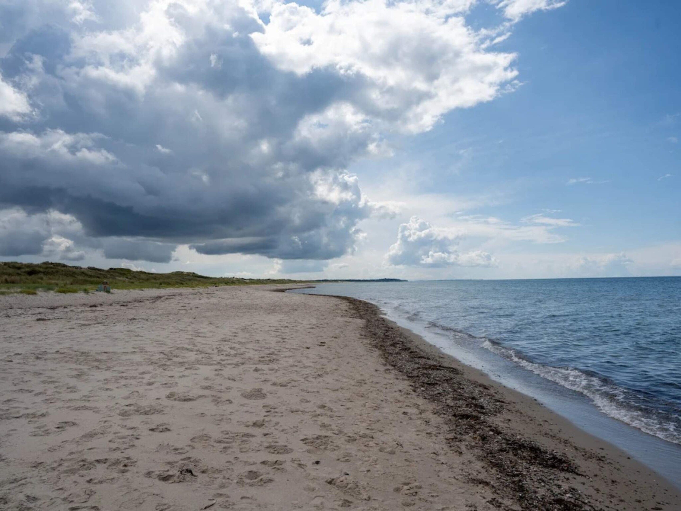 A beach with a sandy shore, a calm sea, and a cloudy sky.