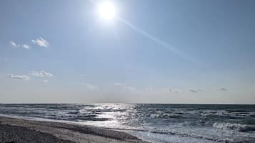 A beach with waves, a clear sky, and the sun shining.