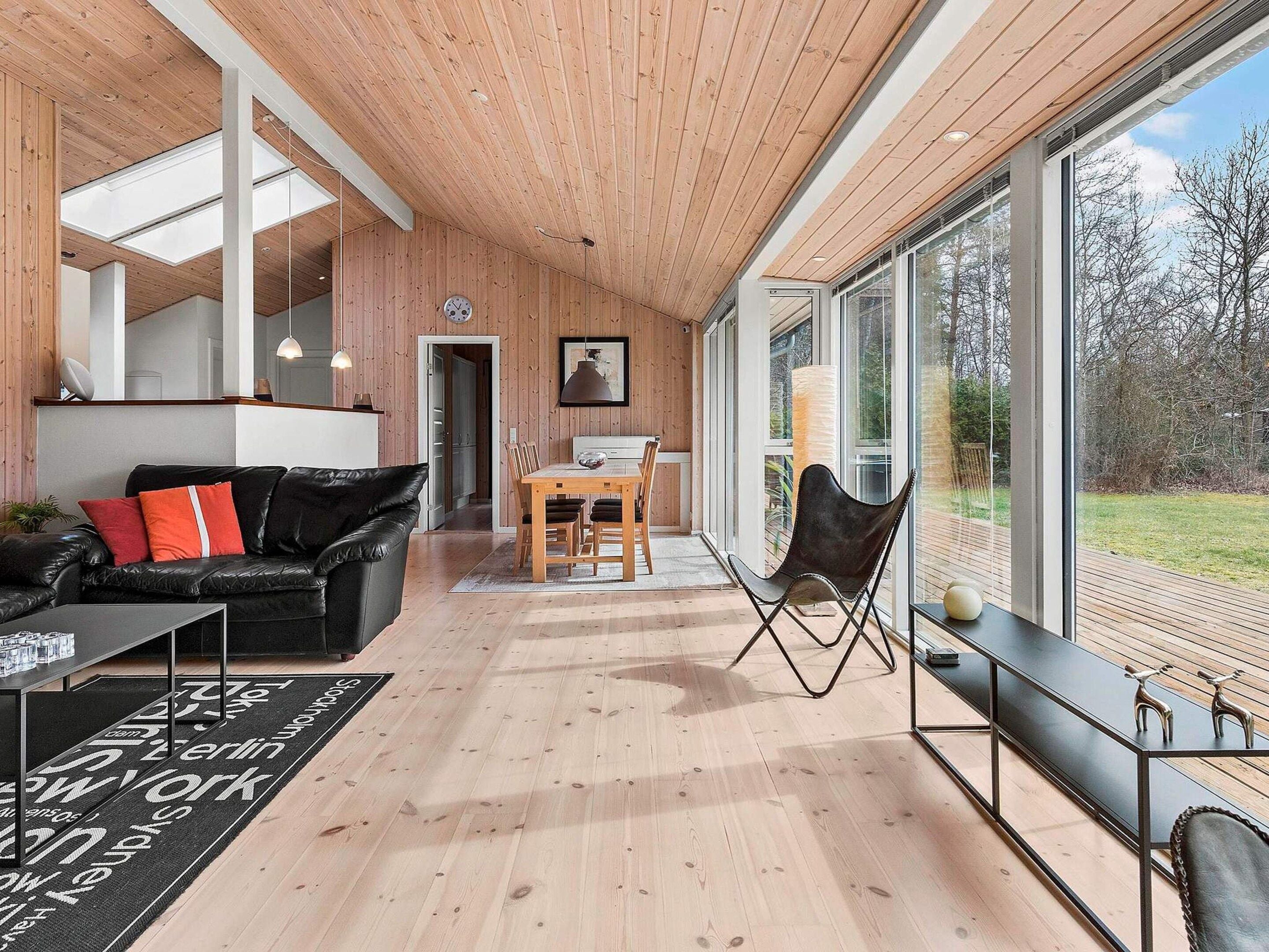Een modern interieur met een houten plafond, een eethoek en grote ramen met uitzicht op het landschap.
