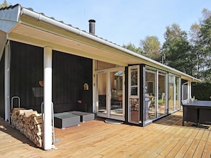 A covered outdoor area with a wooden deck, a glass enclosure, and a stack of firewood. - 4 Star Holiday Home in Frederiksvaerk (Frederiksvaerk)