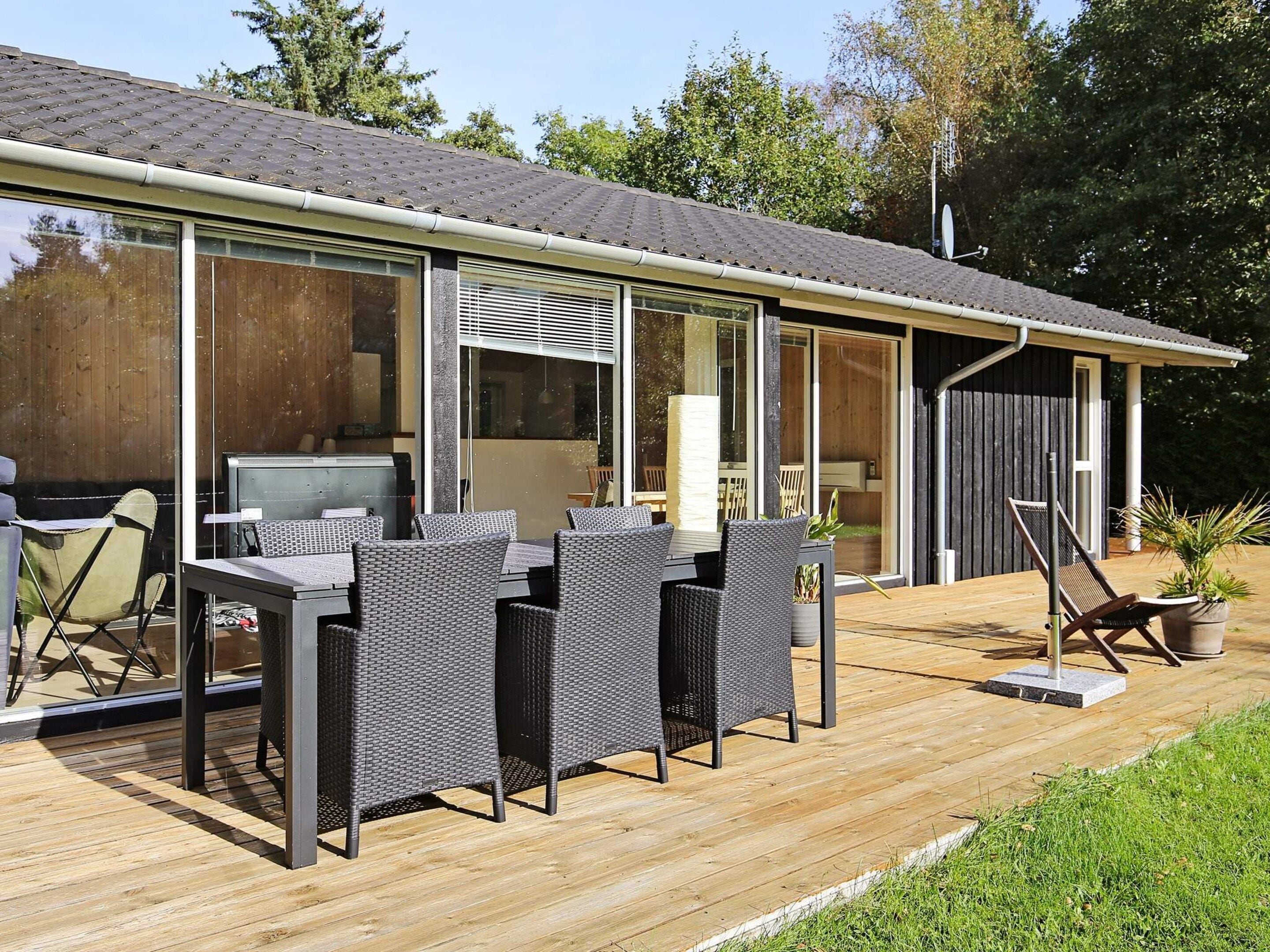 A modern outdoor patio with a dining table and chairs, a television, and a large window overlooking a garden.