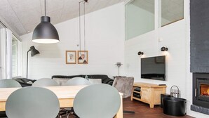 A modern living room with a fireplace, a dining area with chairs, a sofa, and a TV mounted on the wall.