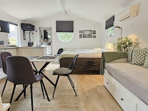 Een compacte, moderne kamer met een bed, een bureau met een computer, een stoel, een bank en een kleine eettafel.