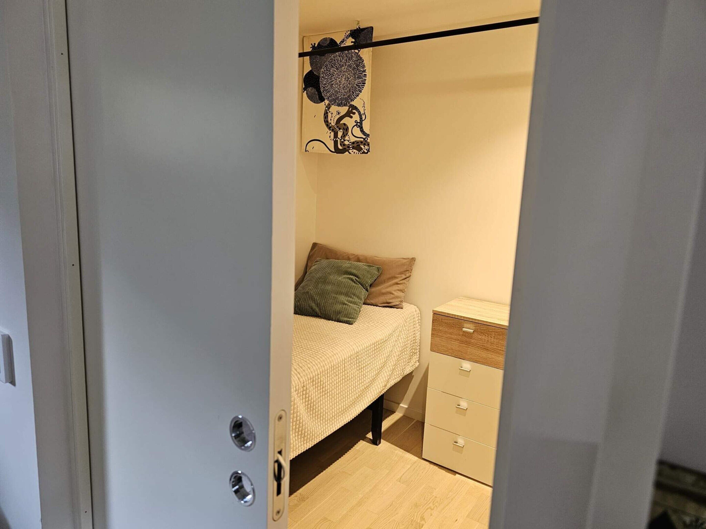 A bedroom with a bed, a nightstand, a dresser, and a wall-mounted shelf with a decorative item.