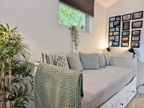 A bedroom with a bed, pillows, a bedside lamp, a window with blinds, a wall with framed pictures, and a potted plant. - 4 Star Holiday Home in Loddekopinge (Loddekopinge)