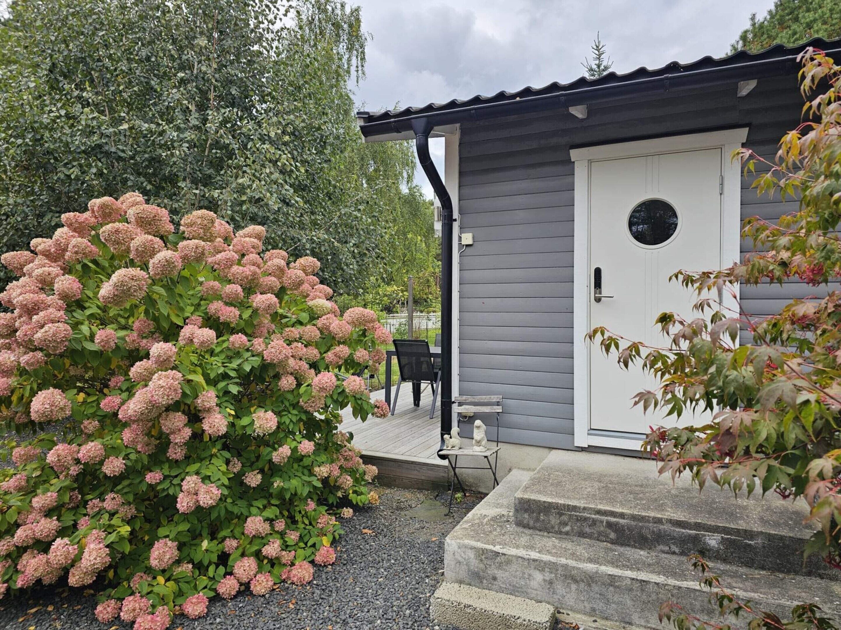 A house with a grey exterior, a white door with a round window, and a small outdoor seating area with a table and chairs.