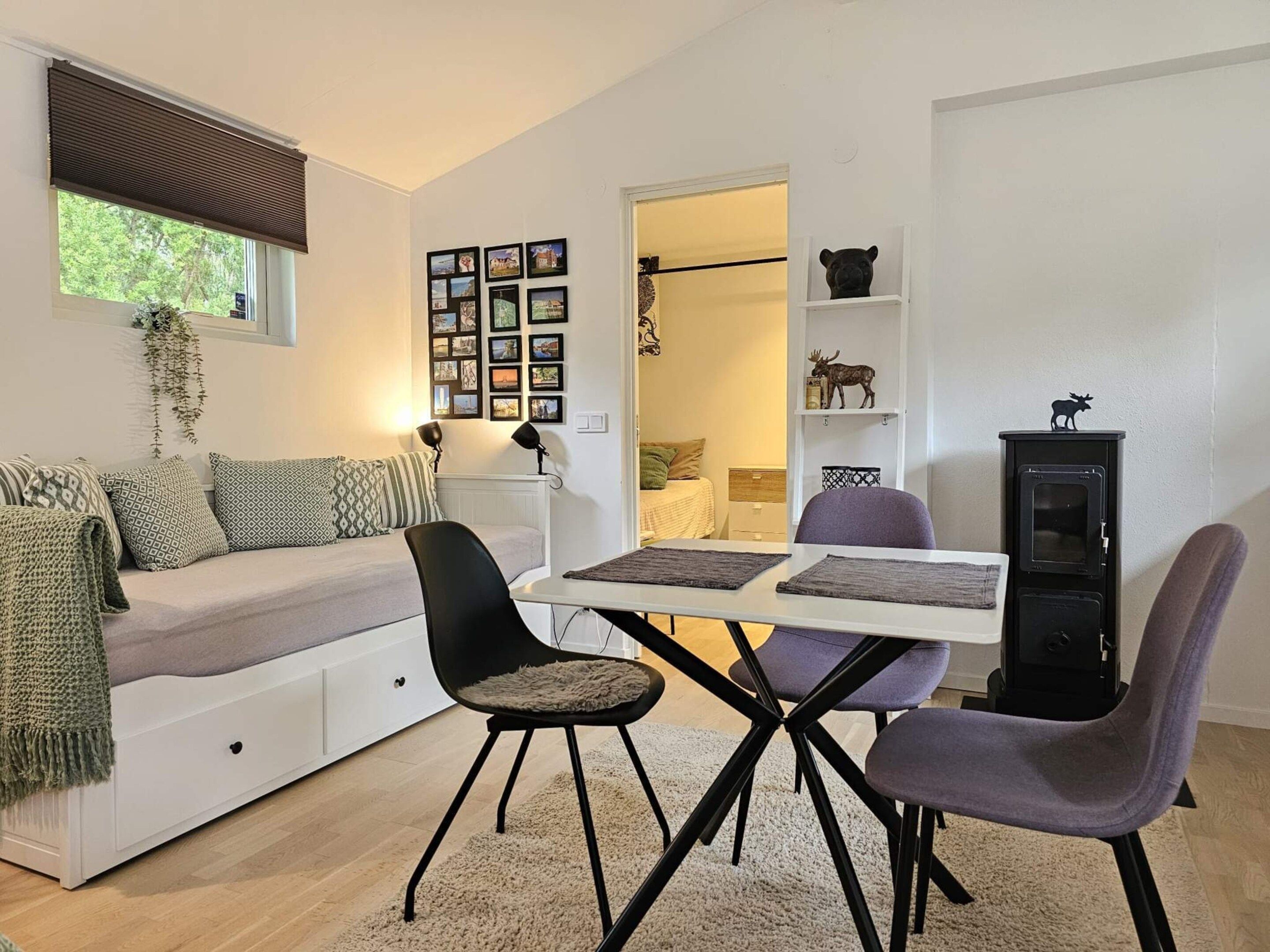 A cozy living room with a sofa, a dining table with chairs, a fireplace, and a wall decorated with framed photos.