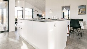Une cuisine moderne dotée d’un îlot central, d’un coin repas avec une table et des chaises, et d’une grande fenêtre qui laisse entrer la lumière naturelle.