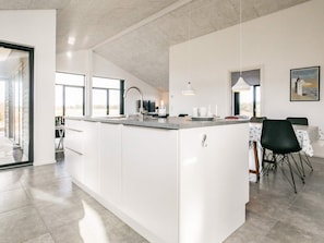 A modern kitchen with a central island, a dining area with a table and chairs, and a large window providing natural light. - 5 Star Holiday Home in Lokken (Lokken)