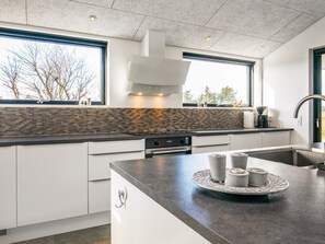A modern kitchen with a large island, stainless steel appliances, and a view of trees outside.