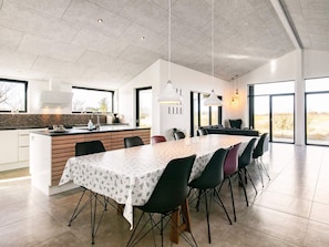 A modern kitchen with a large island, dining area with a table and chairs, and large windows offering views of the outdoors. - 5 Star Holiday Home in Lokken (Lokken)