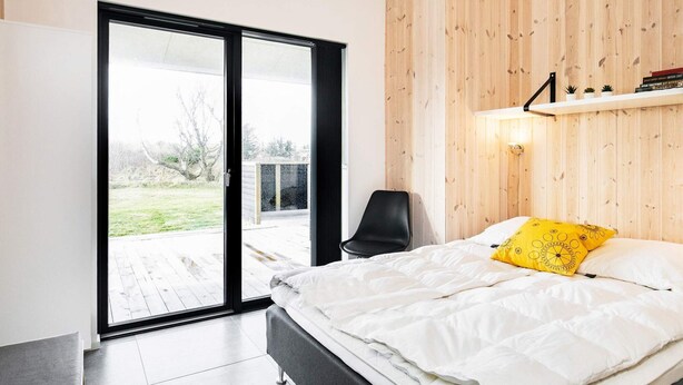 Une chambre moderne avec un lit, une chaise, un mur en bois et une porte-fenêtre coulissante donnant sur un espace extérieur.