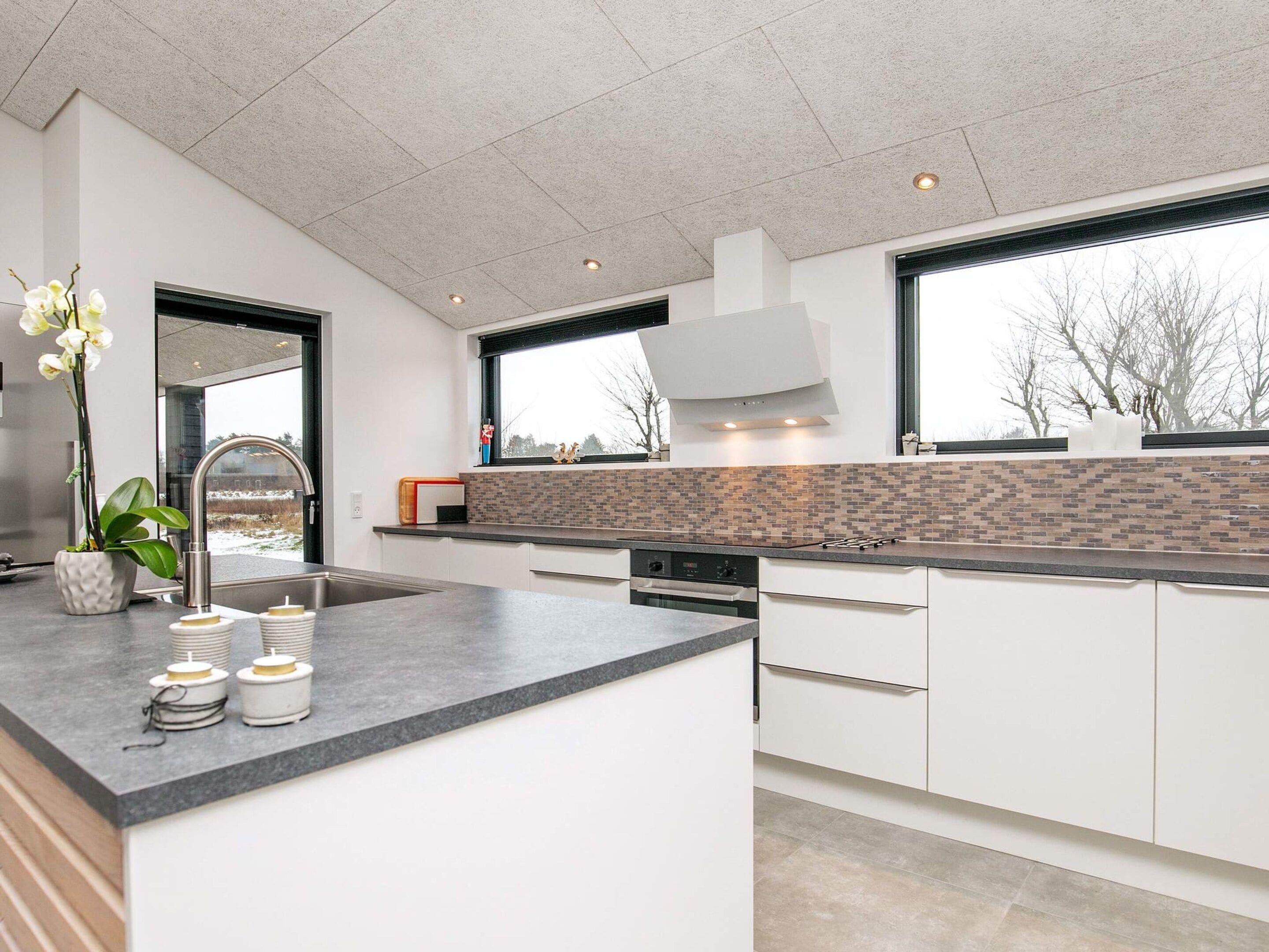 A modern kitchen with a large island, white cabinetry, and a view through the windows.
