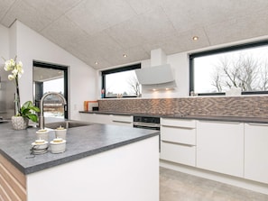Eine moderne Küche mit einer großen Kochinsel, weißen Schränken und Blick durch die Fenster.