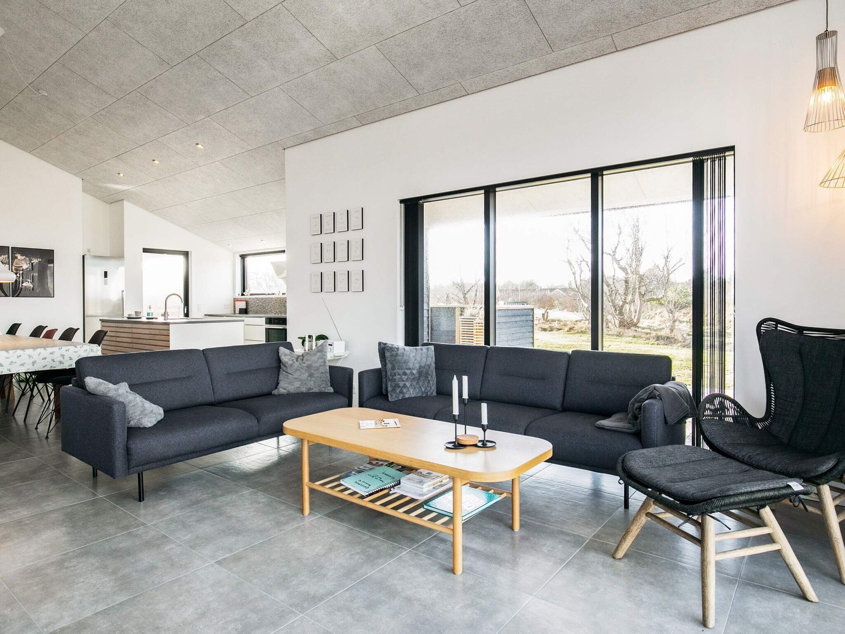Un salon moderne avec un canapé, une table basse et un fauteuil. On aperçoit une cuisine au fond, avec un coin repas.