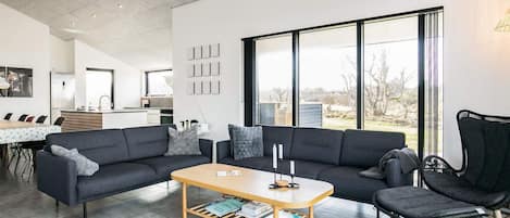 A modern living room with a sofa, a coffee table, and a chair. There is a kitchen in the background with a dining area.
