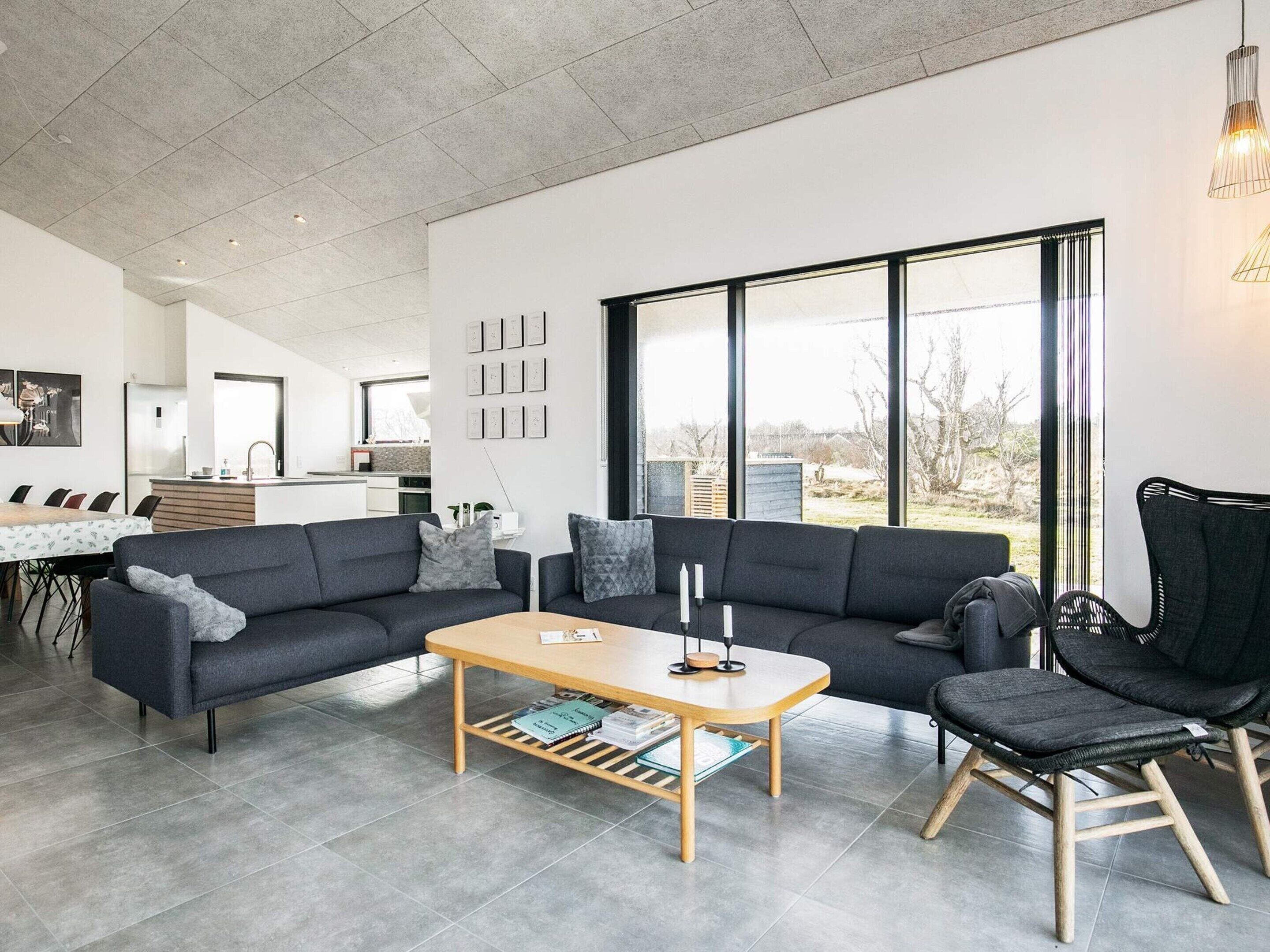 A modern living room with a sofa, a coffee table, and a chair. There is a kitchen in the background with a dining area.