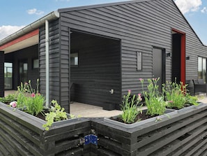 A modern building with a dark exterior, a covered outdoor area with raised garden beds, and a red door. - 5 Star Holiday Home in Lokken (Lokken)