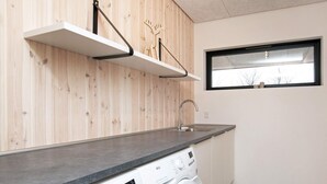 Une cuisine moderne dotée d’un lave-linge encastré, de lambris en bois, d’une fenêtre et d’une étagère en métal.