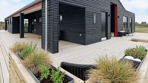 Una casa moderna con un porche cubierto, una puerta roja y fachada negra.