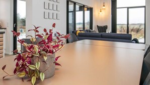 Un intérieur moderne avec une table à manger, une plante en pot, un canapé et de grandes fenêtres.