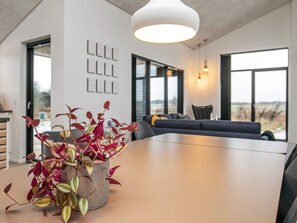 A modern interior with a dining table, a potted plant, a sofa, and large windows. - 5 Star Holiday Home in Lokken (Lokken)