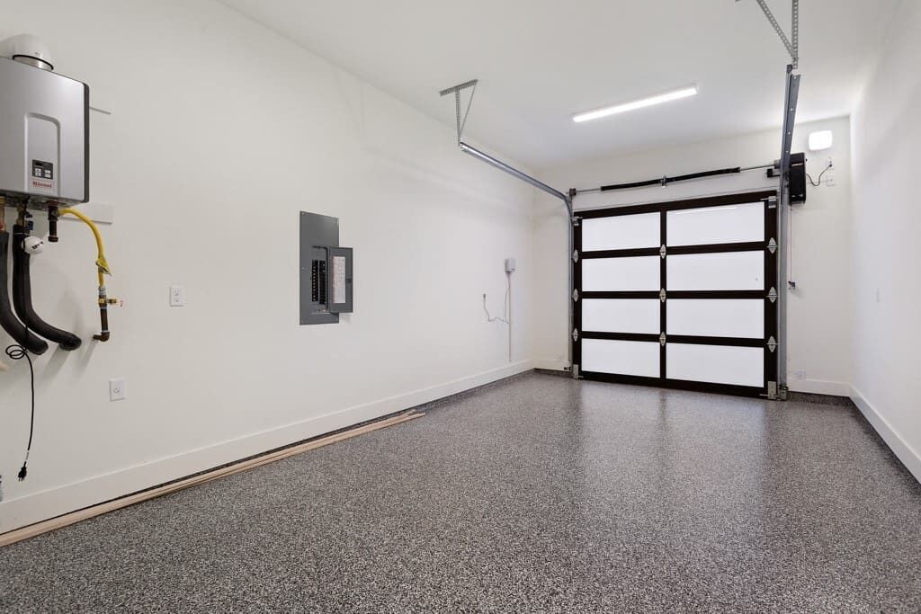 A clean, empty garage with a water heater, a control panel, and a garage door.